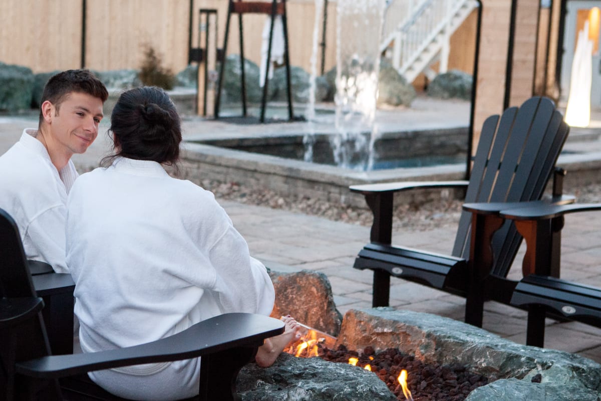 2 people relaxing by a fire outside at the spa.