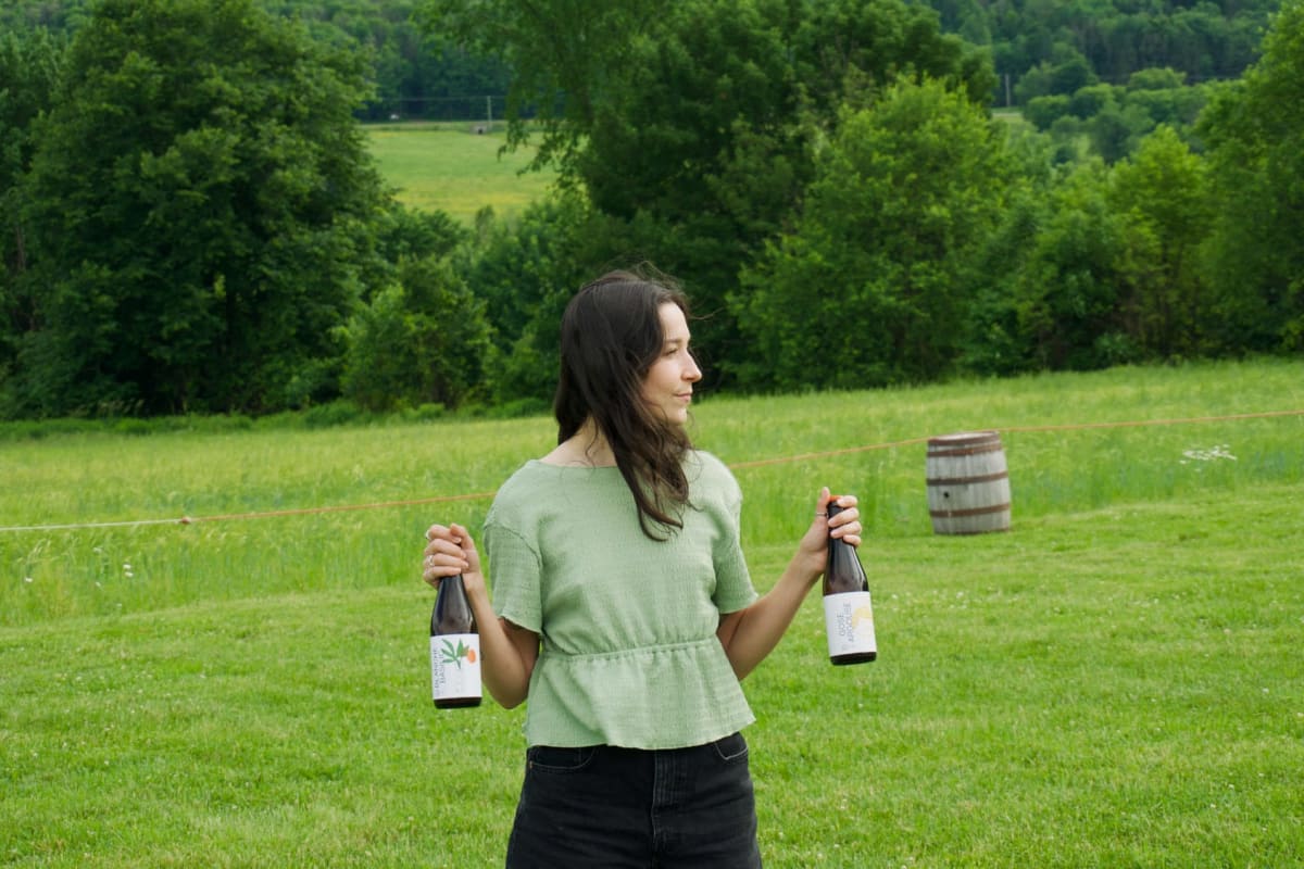 Femme dans un champ qui tient deux bouteilles de vin.