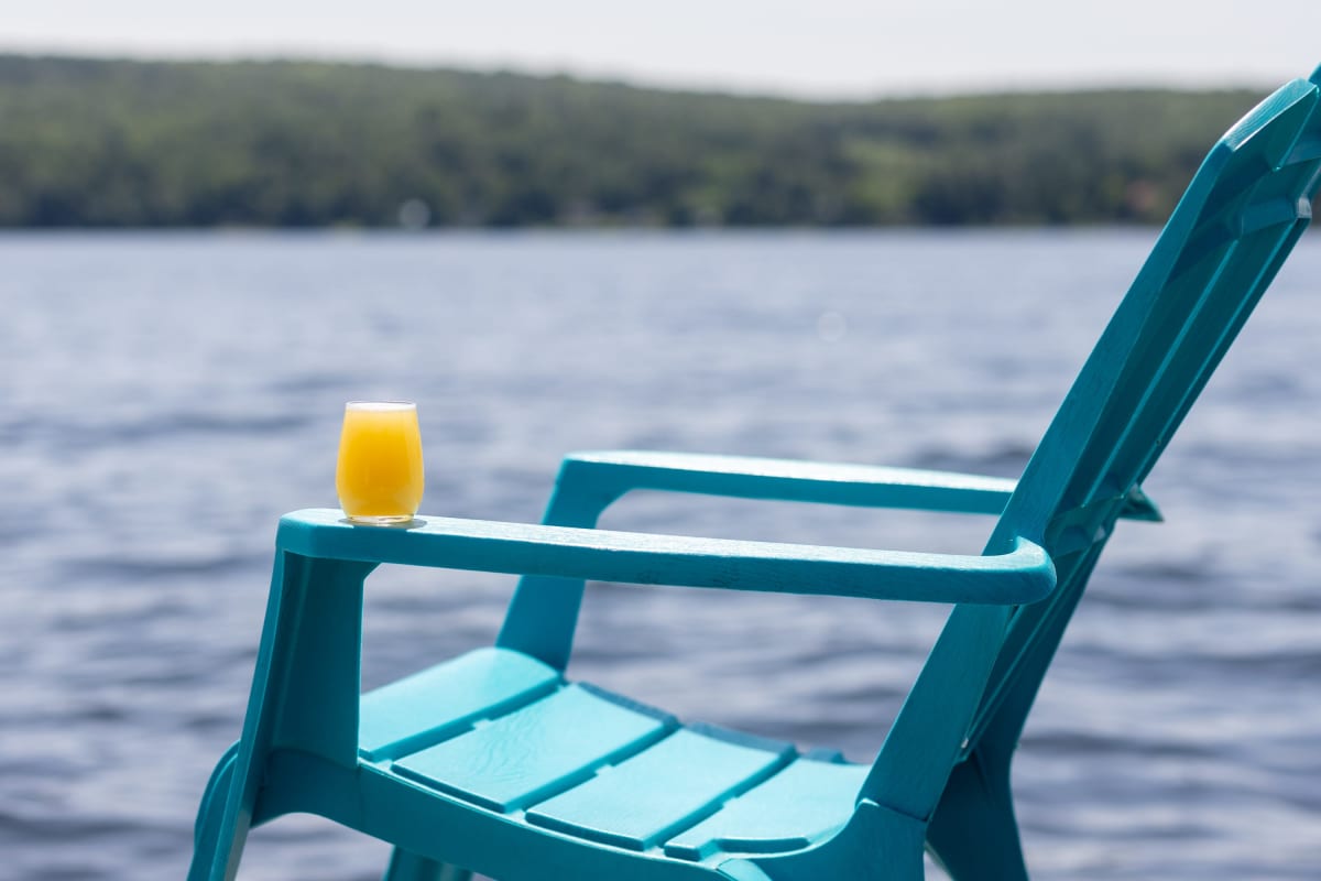 Chaise Adirondack turquoise au bord de l'eau; un cocktail est posé sur l'accoudoir.