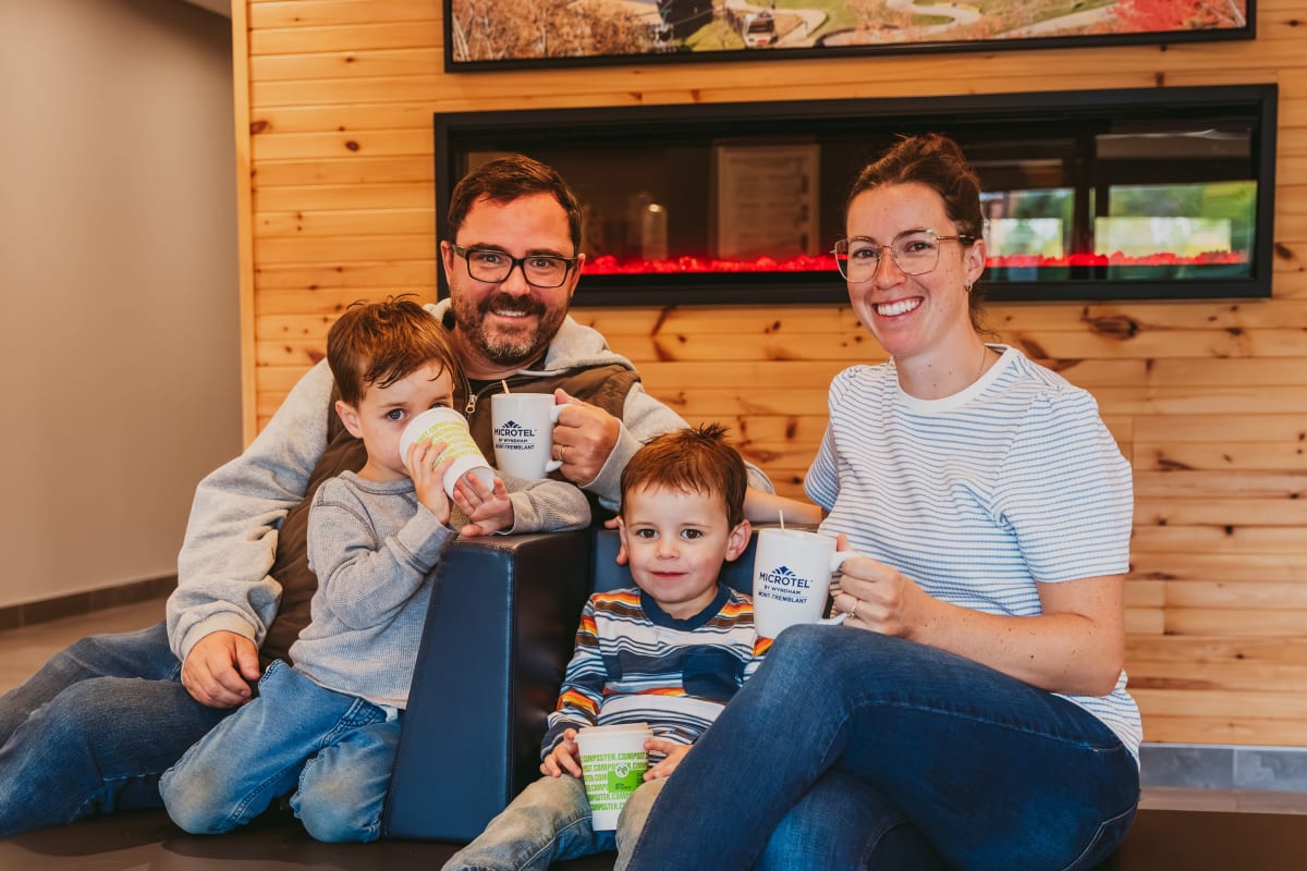 Deux parents et deux enfants souriants, tasse à la main, devant un mur en bois naturel.