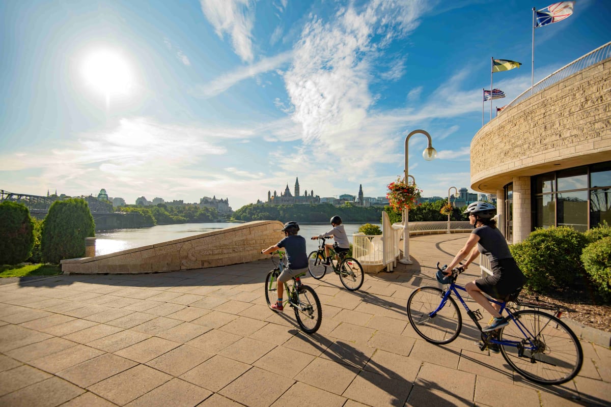 Parent et deux enfants en vélo à l'extérieur du Musée canadien de l'histoire
