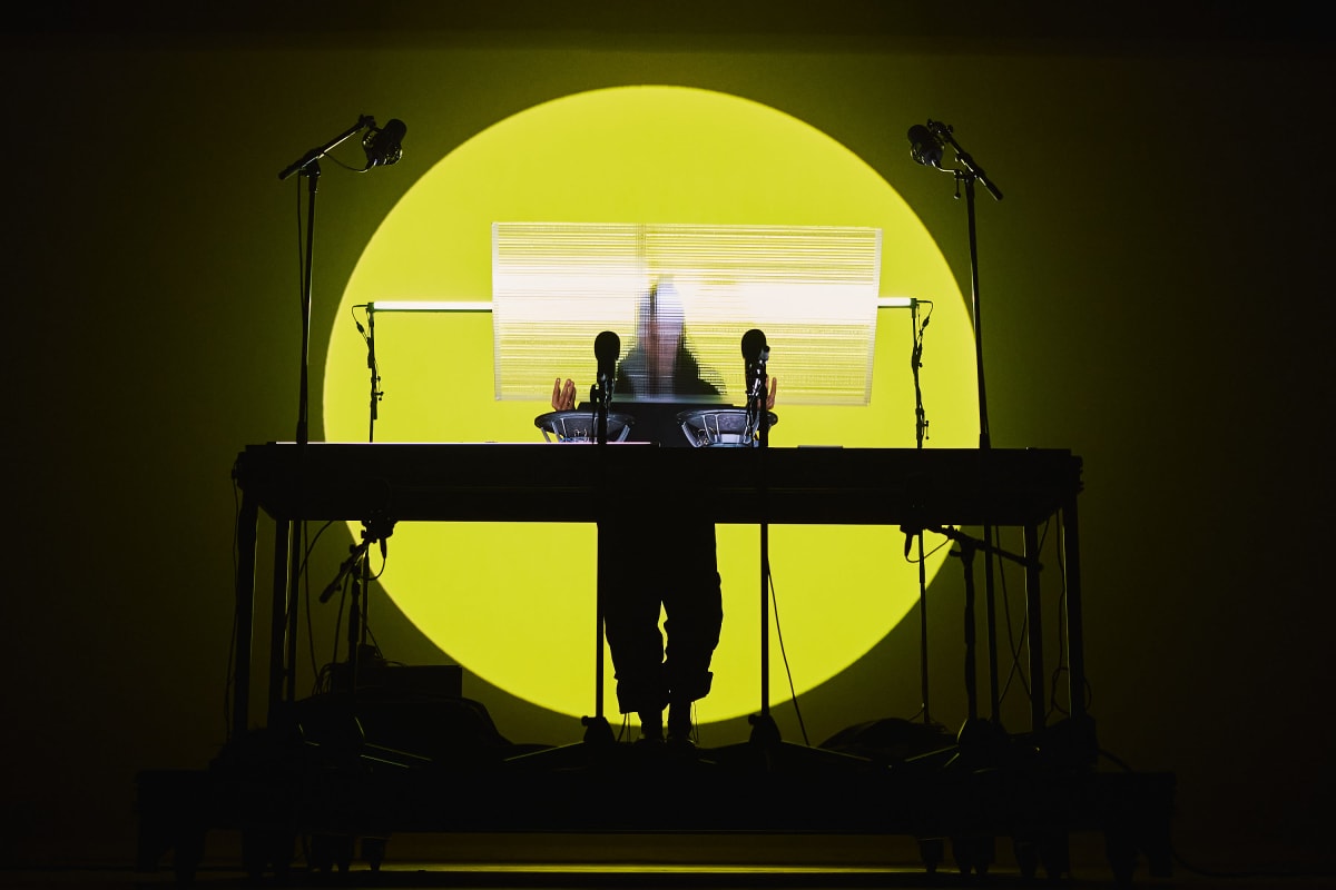 DJ sur une scène, derrière sa table tournante avec un fond lumineux rond jaune soleil