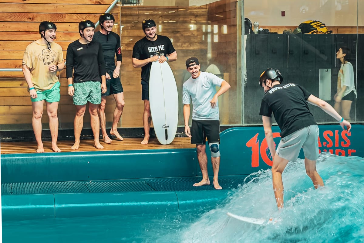 Man surfing in an indoor pool, with a group of people watching