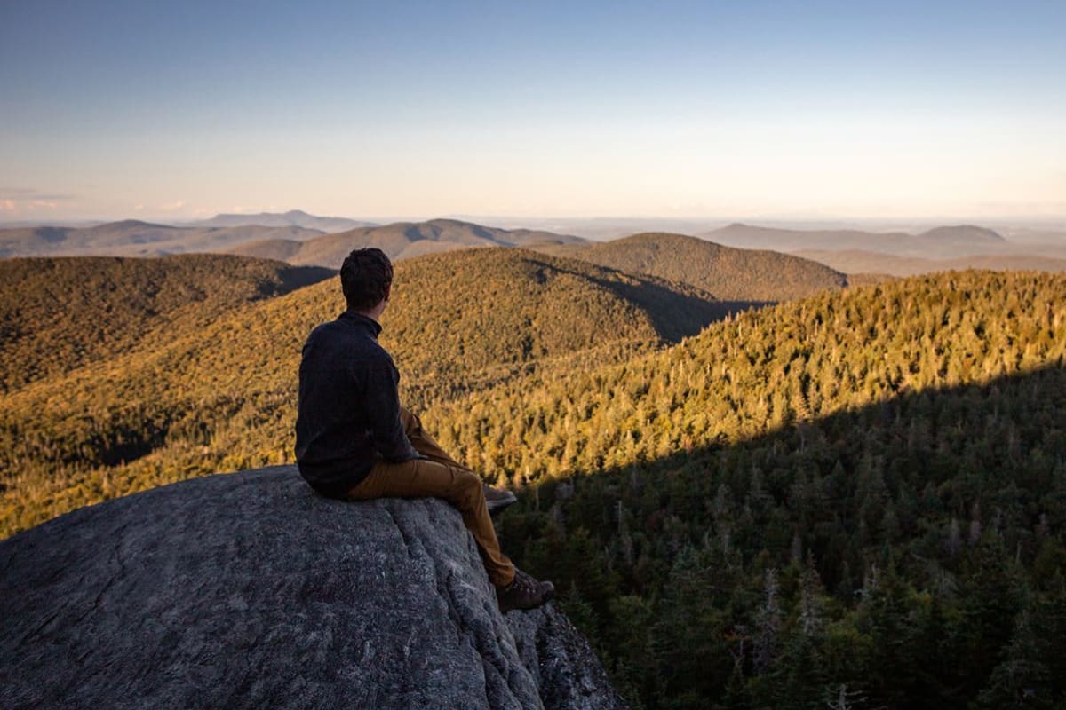 A hiker at the summit in autumn at Parc d'environnement naturel de Sutton.