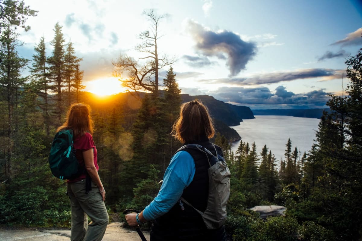 Parc national du Fjord-du-Saguenay - Two women on top of a mountain, forest and sunset in the background.