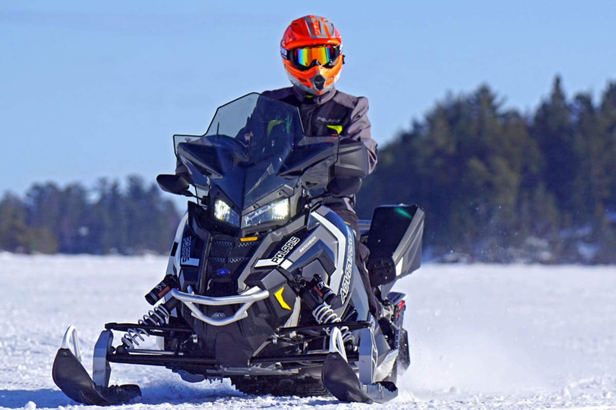 Snowmobiler on a snowmobile on the snow with a forest behind.
