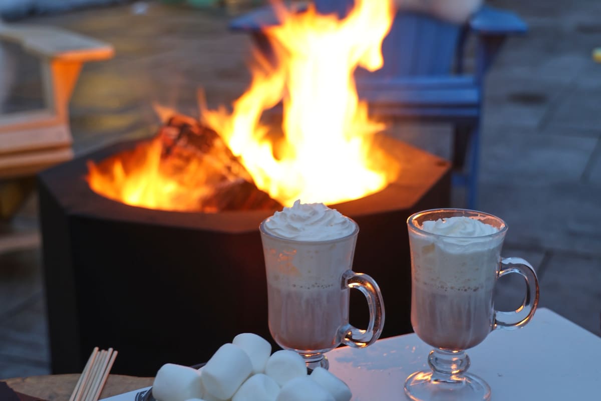 Outdoor firepit with two mugs of hot cocoa and ingredients to make s'mores.