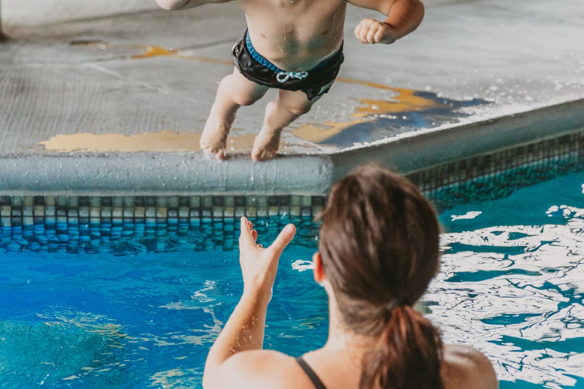 Mother in the hotel pool catching her son jumping in the water.