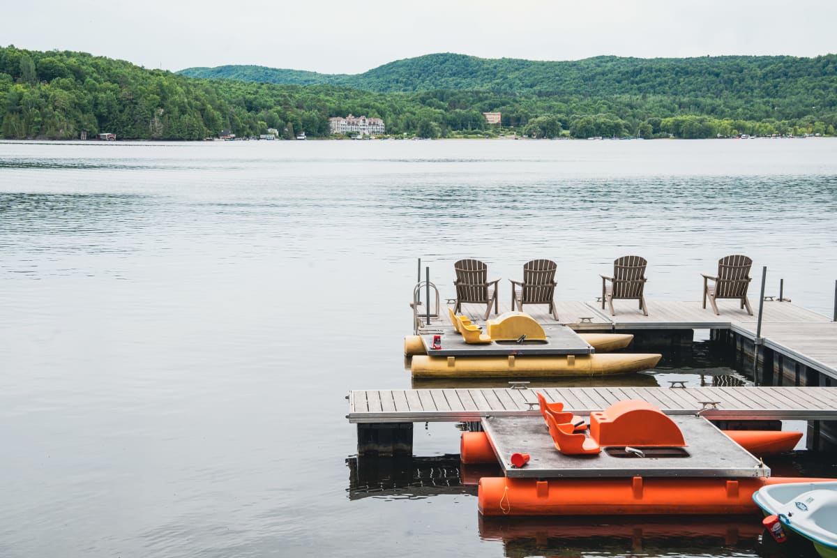 A dock, chairs, and a pedal boat by the lake.