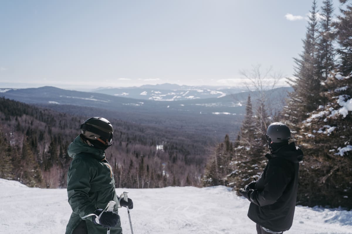 Two people on a ski slope, looking at the landscape.
