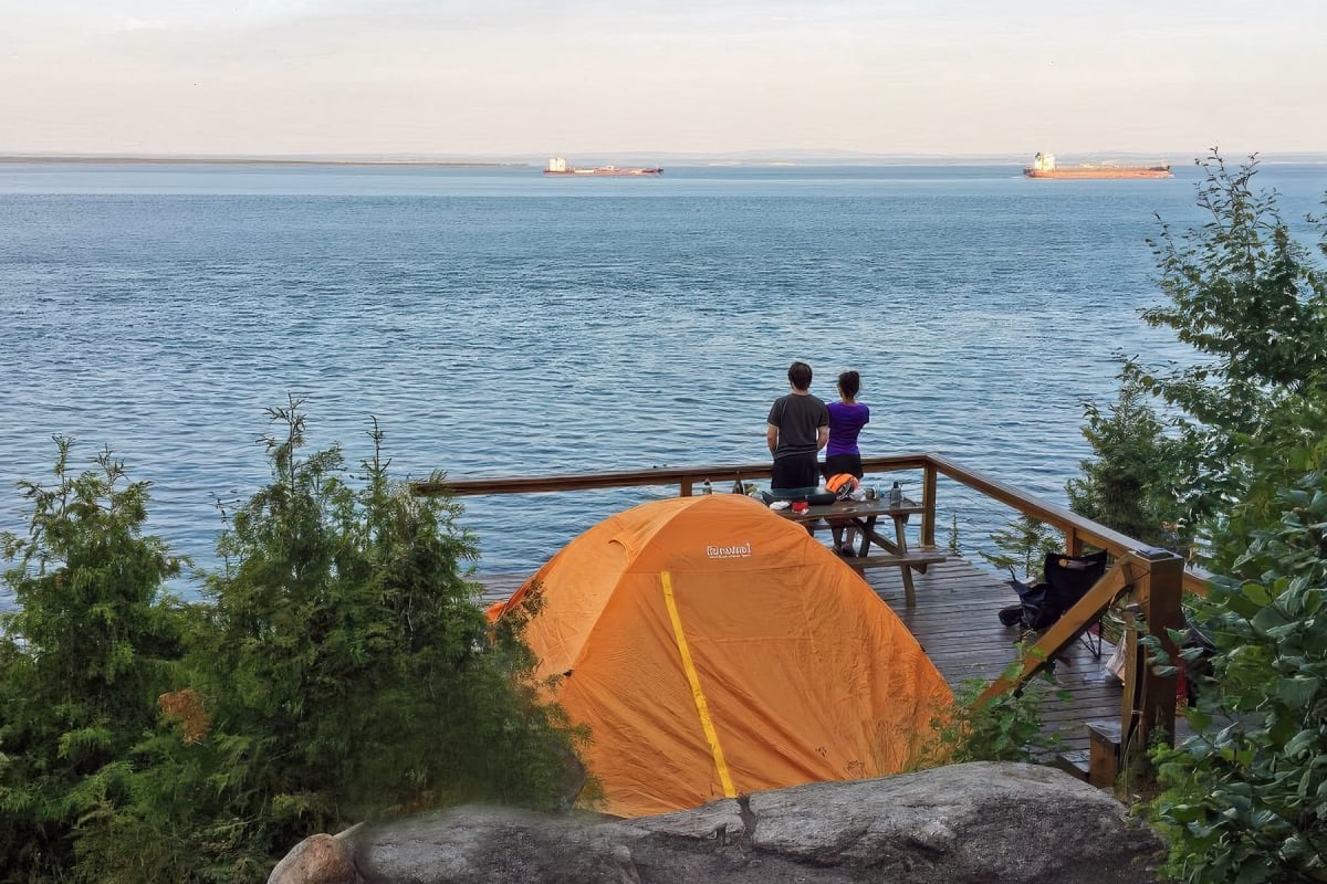 Couple à côté d'une tente qui regarde la mer.