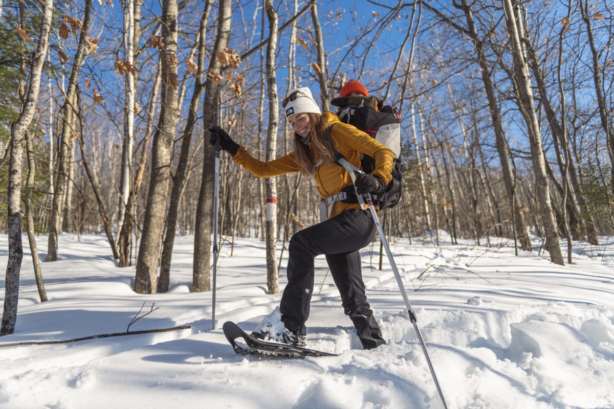 Femme en raquettes dans une forêt dénudée.