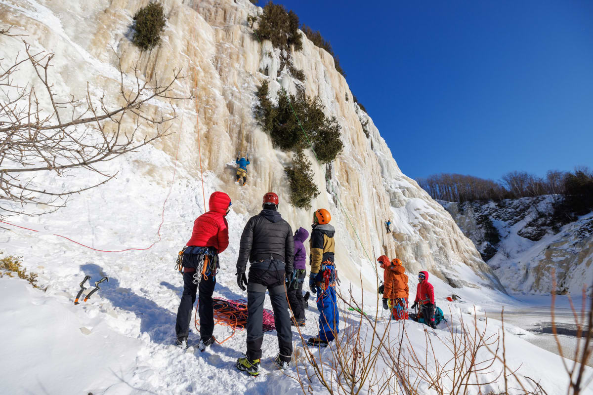 Spectators watch a person climbing an ice wall.