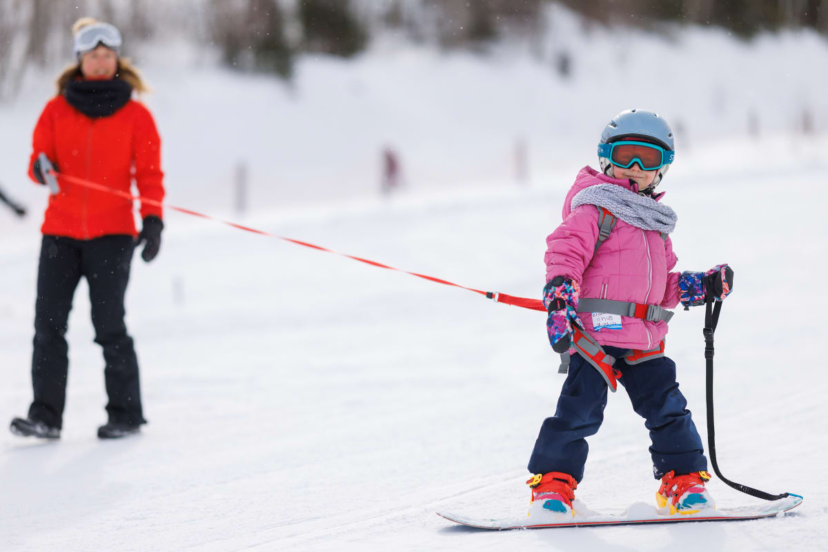 Young girl learning to snowboard with an instructor.