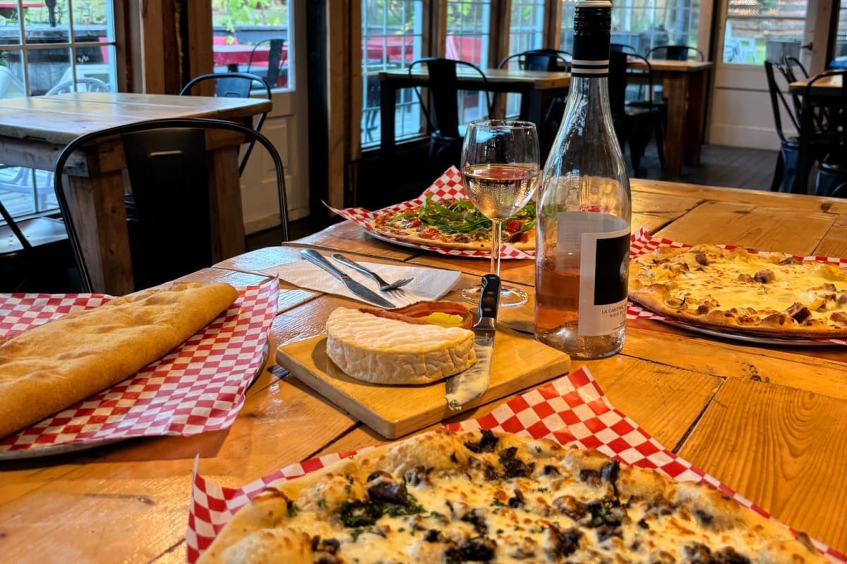 Pizza au jardin - Table en bois sur laquelle sont posées des pizzas et un plateau de fromages.