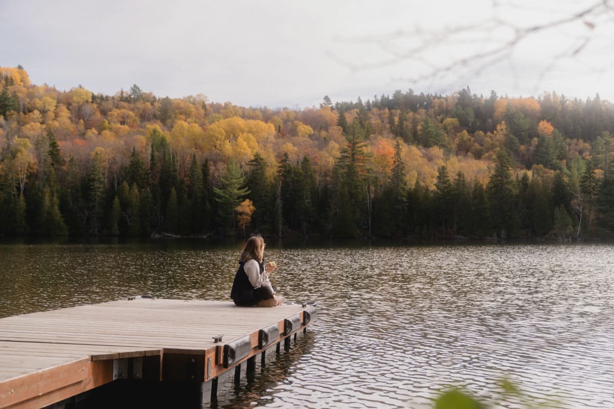 Femme assise sur un quai au bord d'un lac à l'automne.