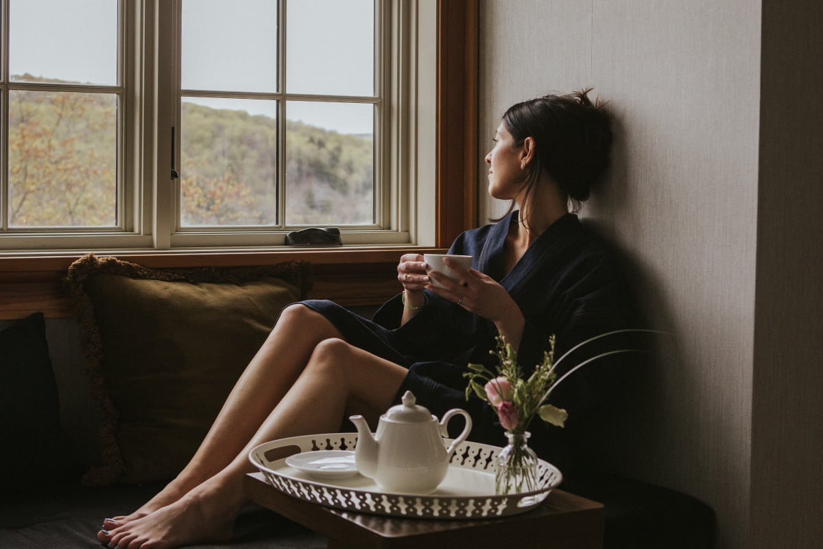 Femme relaxant devant une fenêtre avec un thé.