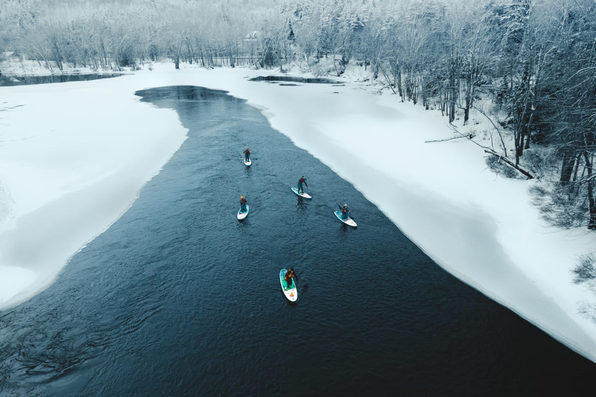 Cinq personnes en SUP des glaces sur un plan d'eau bordé de neige.