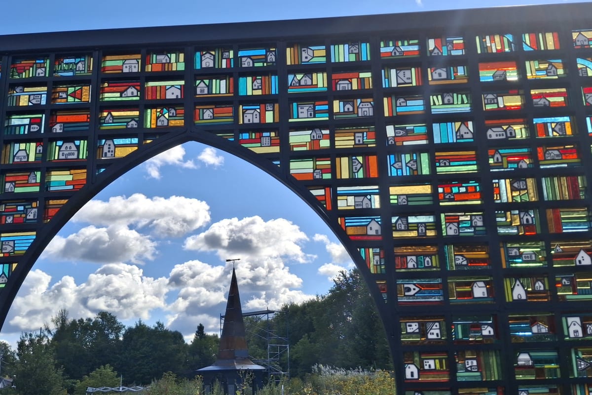 An outdoor art installation consisting of several stained-glass panels arranged to form a rural landscape.