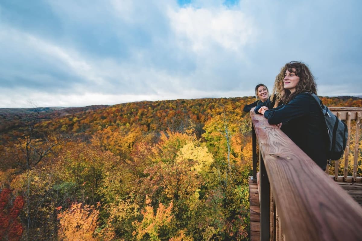 3 women hiking and admiring the fall view from a lookout at Parc des Montagnes Noires de Ripon.