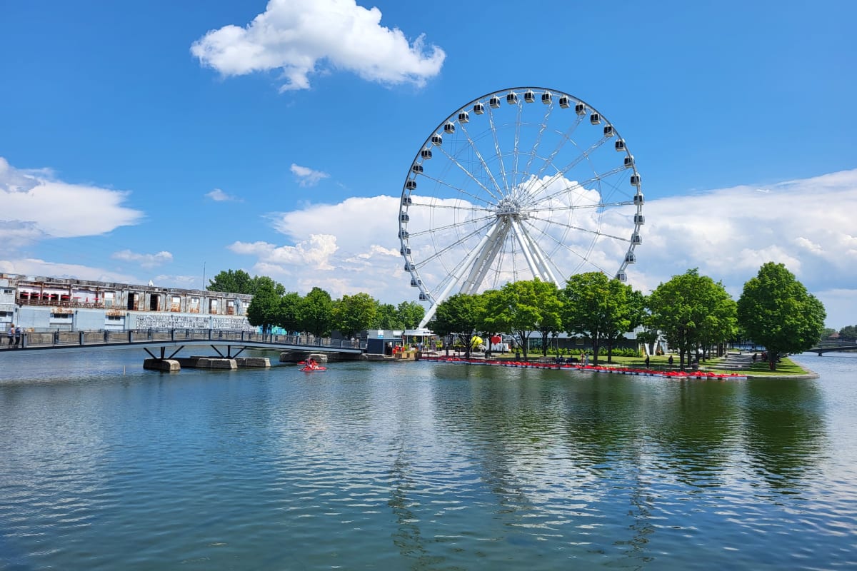 Grande Roue de Montréal vue de loin, avec un plan d'eau à l'avant et un ciel bleuté à l'arrière.