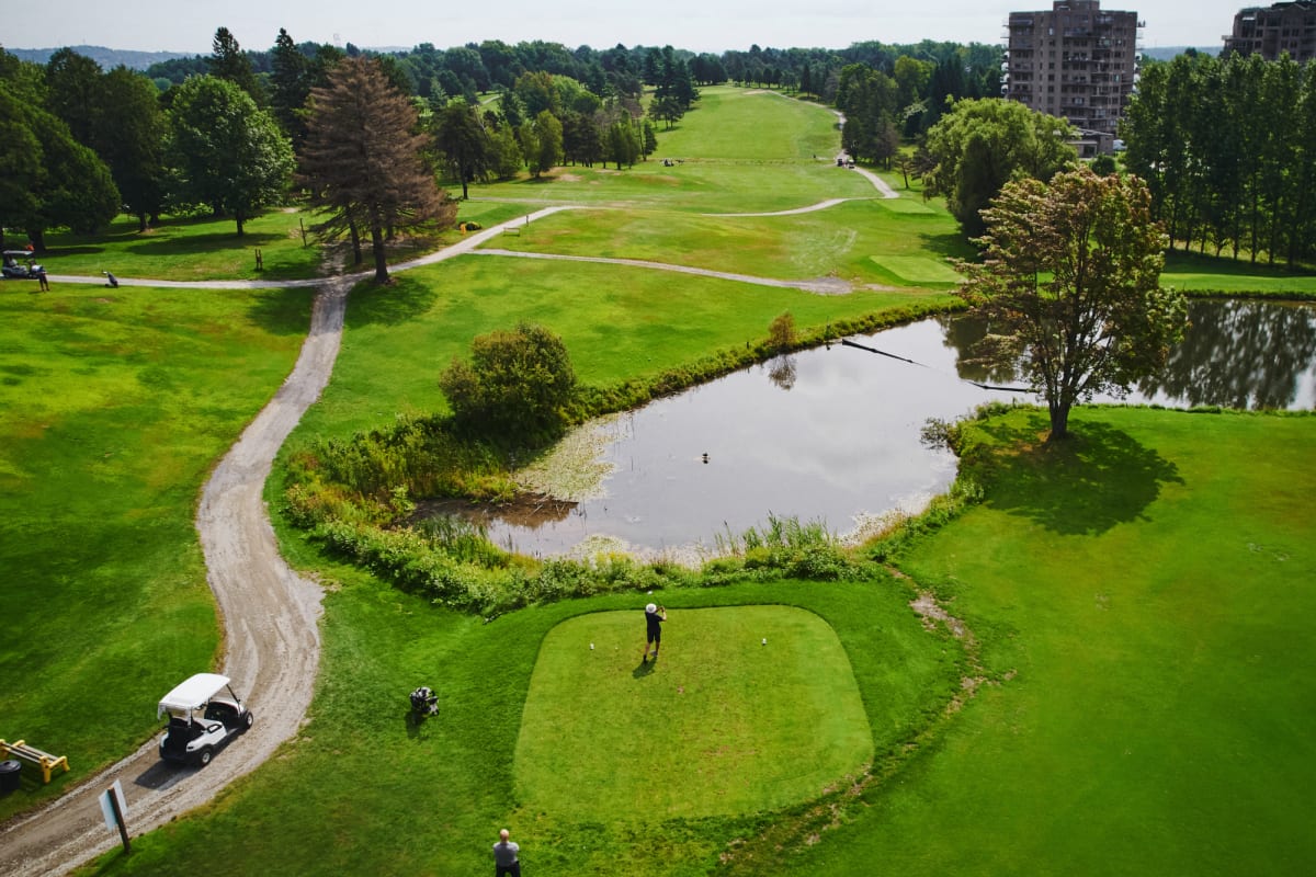 Vue aérienne d'un terrain de golf avec plan d'eau, sentier et voiturette.
