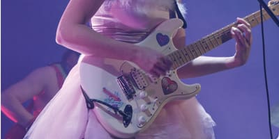 CEM - A woman in a pink dress is singing and playing electric guitar