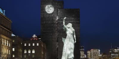 Cité Mémoire - Projection lumineuse d'une statue féminine et d'une lune sur un grand bâtiment sombre, la nuit
