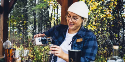 Distillerie du Fjord - Une femme prépare un breuvage alcoolisé, nature en arrière-plan.