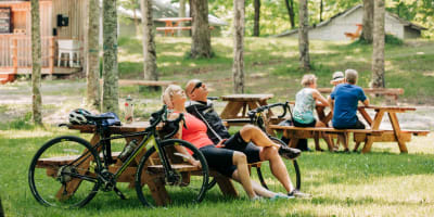 Érablière du Village - A man and a woman are seated at a picnic table, with their bikes leaning against it.
