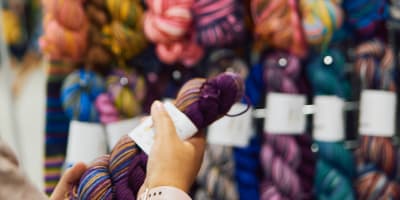 Twist Fibre Festival - A person holds a hank of yarn in front of a display stand.