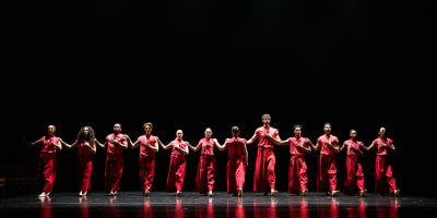 Festival des Arts de Saint-Sauveur - Des danseurs habillés en rouge sont disposés en ligne sur une scène noire