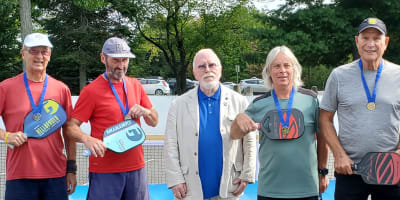 Jeux FADOQ provinciaux - On a pickleball court, there are six men wearing gold medals around their necks, and one man is dressed in a suit.