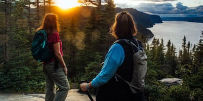 Parc national du Fjord-du-Saguenay - Deux femmes en haut d'une montagne, la forêt et le couché de soleil en arrière-plan.