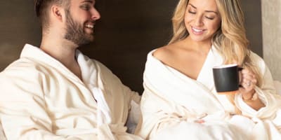 Couple relaxing in bed wearing bathrobes and enjoying a cup of coffee.