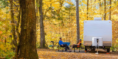 Two people sitting next to an RV in Parc national de la Jacques-Cartier in the fall.