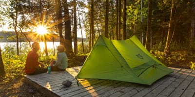Un couple assis à côté d'une tente verte au Parc national du Lac-Témiscouata.
