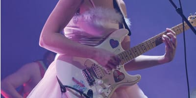 CEM - A woman in a pink dress is singing and playing electric guitar