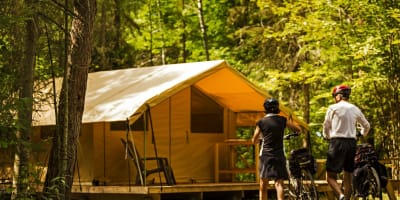 Un couple en vélo en direction d'un prêt-à-camper du Centre touristique du Lac-Kénogami.