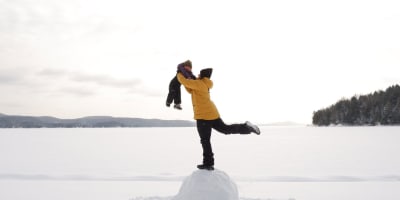 A parent holding their child in the air at the Centre touristique du Lac-Simon, in winter.