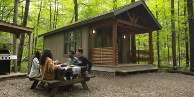 Des personnes assises à une table de pique-nique à côté d'un chalet au Parc national d'Oka.
