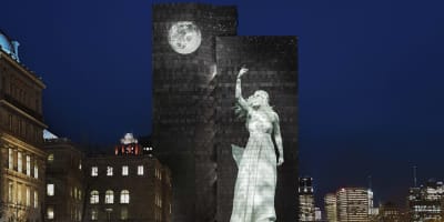 Cité Mémoire - Light projection of a woman and a moon on a large dark building, at night