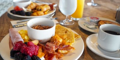 Two lunch plates filled with fruit, bacon and potatoes. 
