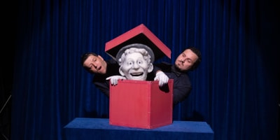 Festival international des arts de la marionnette - Une marionnette est dans une boîte rouge. Deux hommes sont à côté.