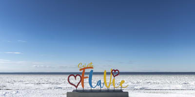 Colorful Sainte-Flavie sign with hearts in front of a snowy Gaspésie landscape.