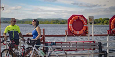 A man and a woman are standing beside the water, with their bicycles at their sides.
