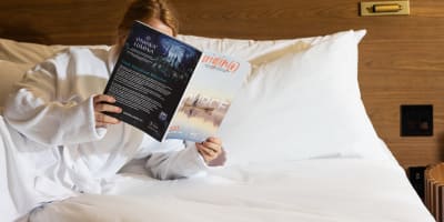 A person reading a book in a hotel bedroom.