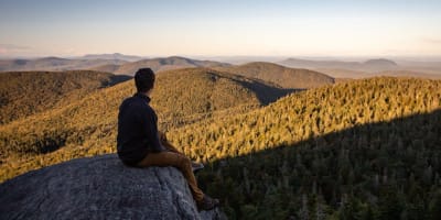 A hiker at the summit in autumn at Parc d'environnement naturel de Sutton.