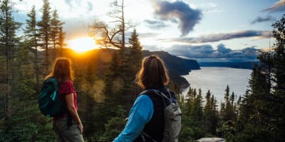 Parc national du Fjord-du-Saguenay - Deux femmes en haut d'une montagne, la forêt et le couché de soleil en arrière-plan.