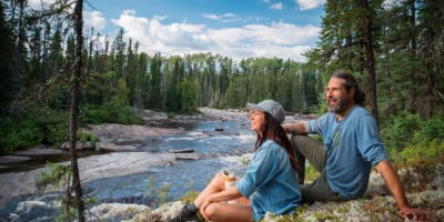 A man and a woman sitting by the river in the summer. 